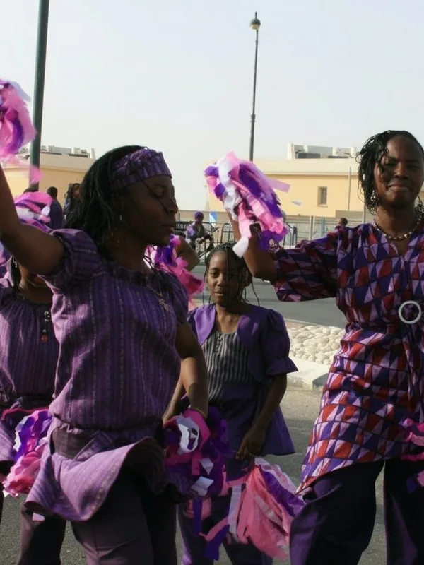 Women dancing in purple outfits with pompoms at a Village of Peace celebration