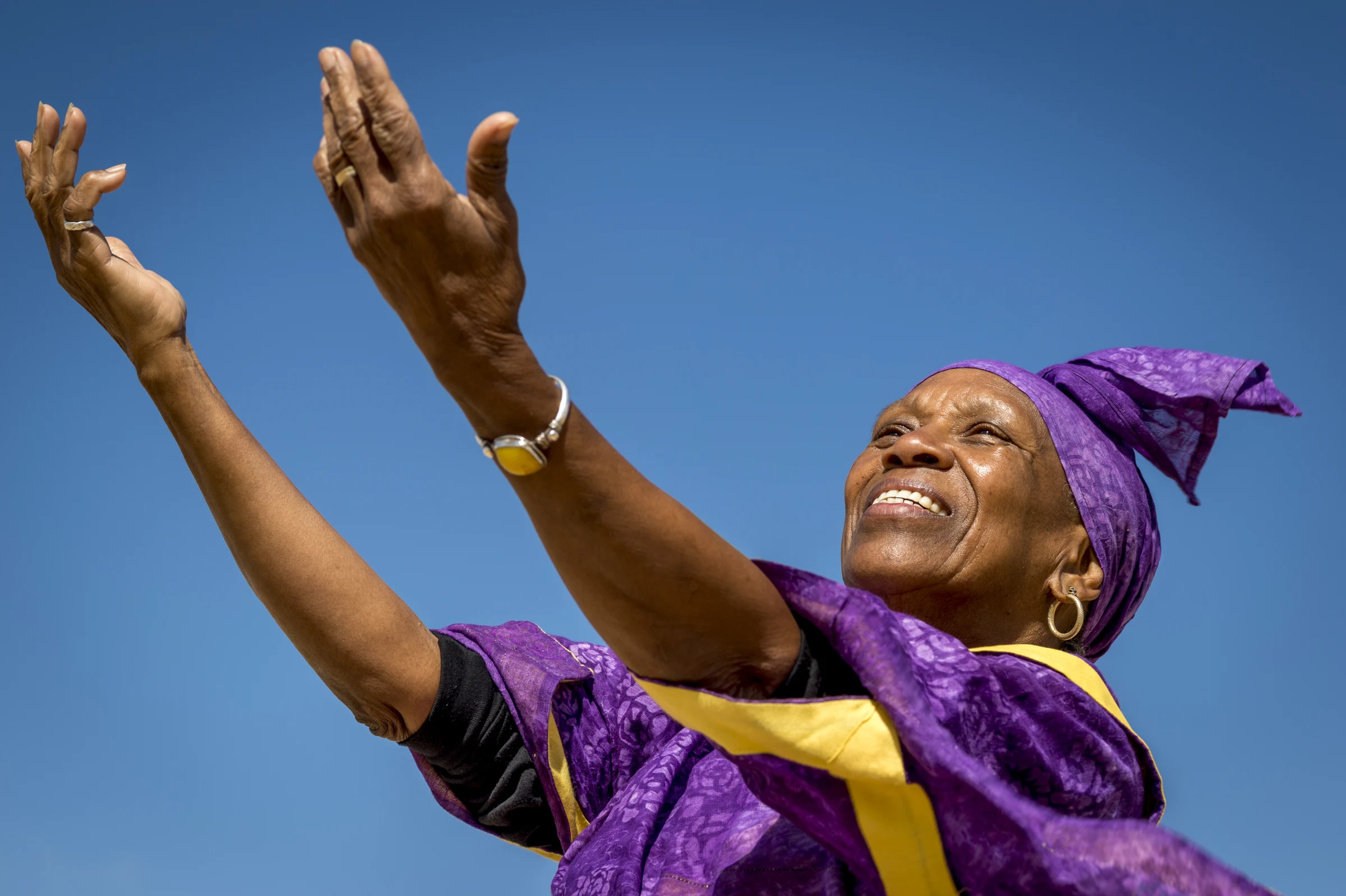 An elder of the Village of Peace community, arms raised joyfully to a clear sky in the Negev, Dimona